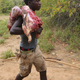 Hadza hunter walking back to camp with a dispatched porcupine flung over his shoulder.